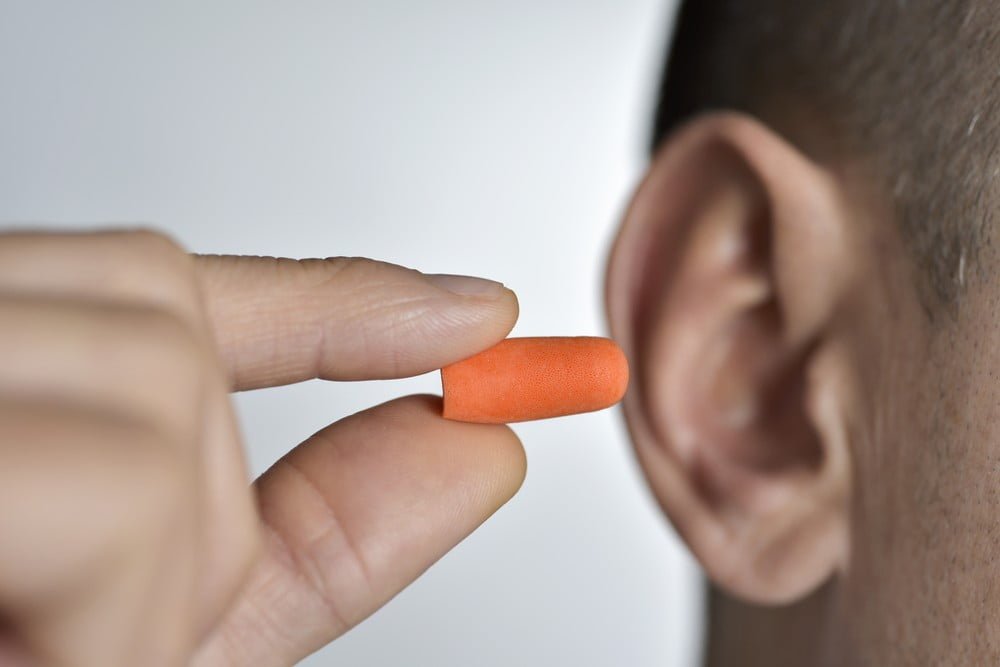 close-up of a young caucasian man inserting an orange ear plug