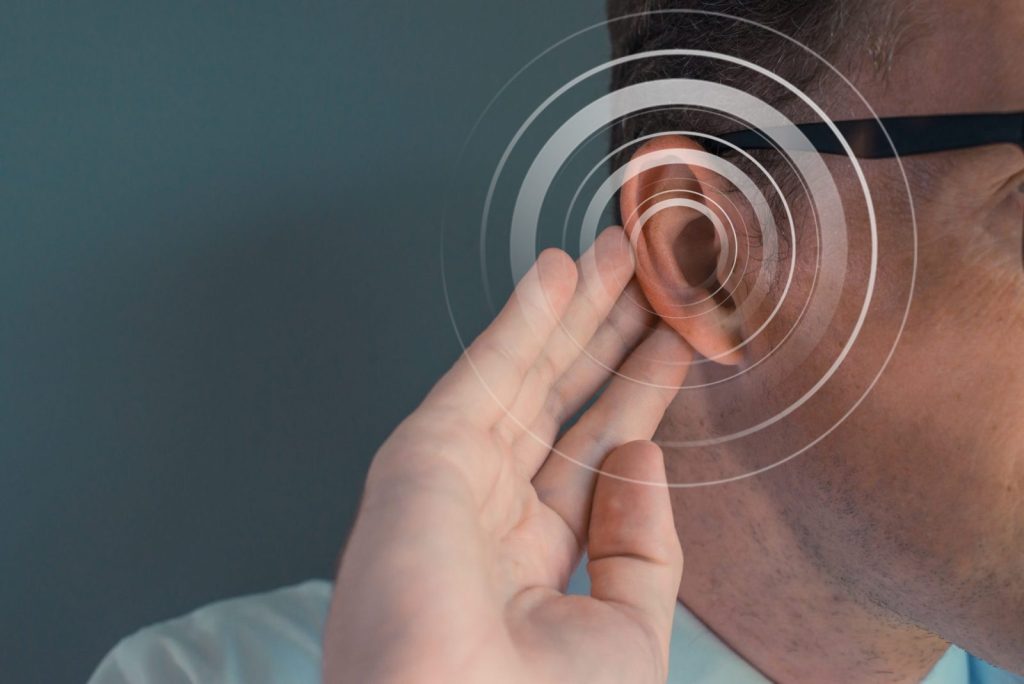 A person touches their ear with sound waves graphic, symbolizing a hearing consultation for potential ear wax removal or hearing aid fitting.