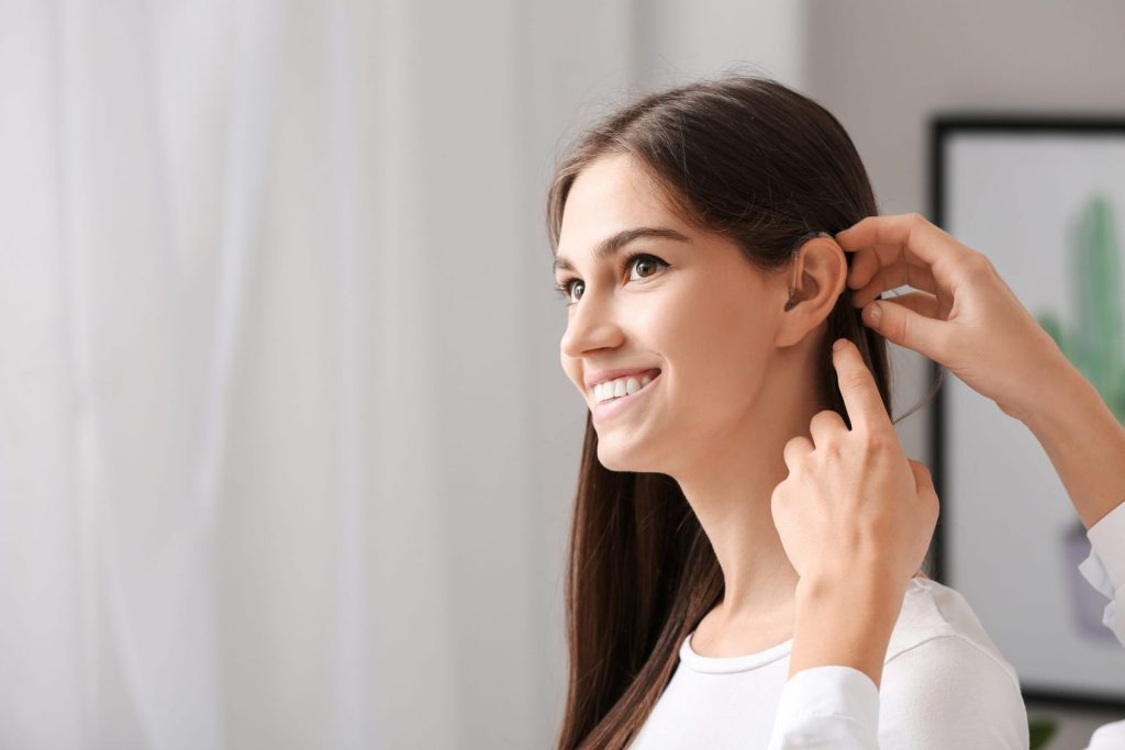 Smiling woman receiving a new hearing aid during an audiology service appointment, symbolising a step towards improved hearing.