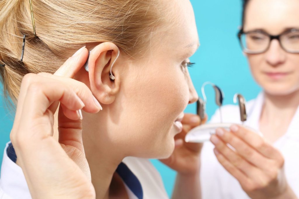 A woman is inserting a hearing aid with guidance from an audiologist