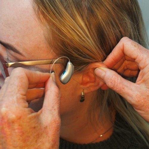 A close-up of a person fitting a behind-the-ear hearing aid